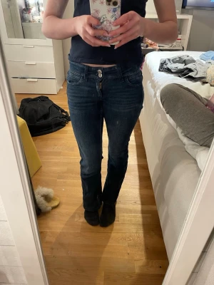 Mörkblå bootcut jeans - Säljer ett par mörkblå bootcut jeans med klassisk femficksdesign och snygga sömmar på bakfickorna. Jeansen har normal midja och är tillverkade i stretchigt denimtyg för skön passform. Perfekta till vardagslooken och lätta att matcha med olika toppar.