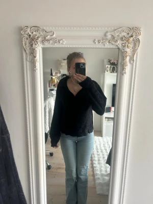 Svart stickad tröja från MQ - Mjuk och fluffig svart stickad tröja från MQ, har jag för mig,  med krage och v-ringning. Tröjan har långa ärmar och en avslappnad passform, perfekt för att hålla sig varm under kyliga dagar. 