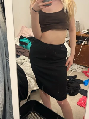 Svart pennkjol i klassisk modell - Säljer en svart pennkjol med hög midja och smal passform. Kjolen är knälång och har en stilren, enkel design utan synliga detaljer. Perfekt till både crop tops och skjortor för en clean look.