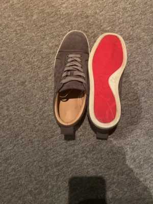 Christian Louboutin - Snygga gråa sneakers i mocka från Christian Louboutin med klassisk röd sula och vita kanter. Skorna har gråa skosnören och en stilren, låg profil.  Skorna är i bra skick. Priset går att diskutera!