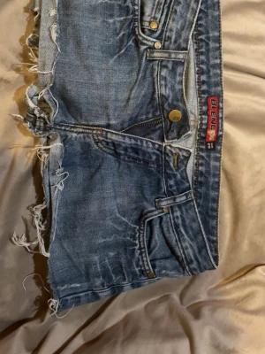 Blå jeansshorts från Blend - Säljer ett par blå jeansshorts från Blend med råa, fransiga kanter och klassisk femficksdesign. Shortsen har gylf med dragkedja och knapp, samt detaljerade sömmar på bakfickorna. Perfekta för en avslappnad stil och snygg stil i sommar💗 Storlek 29