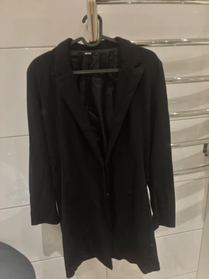 Svart kavaj från Bik Bok - Stilren svart kavaj från Bik Bok med klassisk krage och helfodrad insida. Rak passform och långa ärmar, perfekt för en snygg och enkel look. Materialet är slätt och ger en clean känsla.