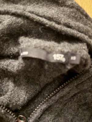 Mörkgrå zip-hoodie från 157 - Mysig mörkgrå hoodie från 157 med dragkedja framtill och huva. Tröjan har ribbade detaljer längs hela plagget och långa ärmar. Perfekt för lager på lager och chill dagar.