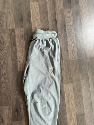 Gråa träningsbyxor från Nike - Snygga grå träningsbyxor från Nike med diskret logga på låret. Byxorna har resår i midjan med dragsko och sidofickor. Tillverkade i mjukt material som passar perfekt för chill eller träning. Smal passform med muddar vid bensluten.