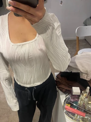 Vit långärmad ribbad topp - Trendig vit långärmad topp med ribbad struktur och fyrkantig ringning. Tunn och lätt material som ger en snygg och modern look. Perfekt att styla med både jeans och kjol.