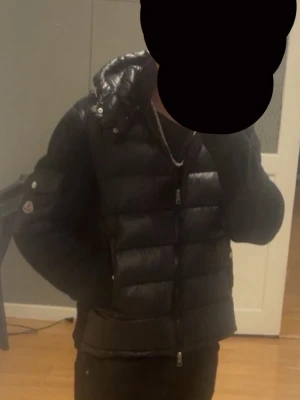  Moncler dunjacka - Snygg svart dunjacka från Moncler med glansig finish, huva och ribbstickade ärmar. Jackan har dragkedja framtill, fickor och Moncler-logga på ärmen. 
