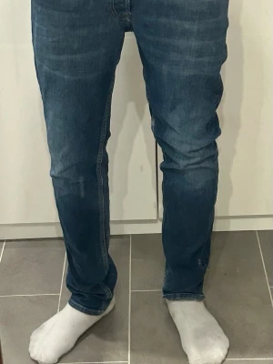 Blå jeans med raka ben - Snygga blå jeans med raka ben och klassisk femficksdesign. Jeansen har en mörk tvätt med lätt slitning och kontrastsömmar på bakfickorna. Tillverkade i denim med en skön passform som funkar till det mesta. Liten defekt där man har skärpet men det är inget man märker