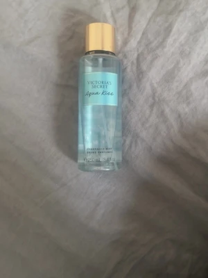 Victoria's Secret Aqua Kiss mist - Fräsch body mist från Victoria's Secret i doften Aqua Kiss. Flaskan är genomskinlig med ljusblå etikett och har ett elegant guldigt lock. Innehåller 250 ml och har en lätt, fräsch doft som känns somrigt ren. Perfekt att spraya på kroppen för en uppfriskande känsla.