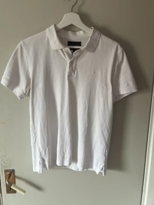 Vit pikétröja från Bondelid - Klassisk vit pikétröja från Bondelid med krage och knappar framtill. Tillverkad i mjuk bomull och har korta ärmar. Diskret broderad logga på bröstet. Perfekt till jeans eller shorts för en clean och enkel stil. S men passar till M