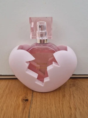 Ariana Grande hjärtformad parfym - Säljer en söt parfym från Ariana Grande med en unik hjärtformad flaska i rosa glas och ett ljusrosa, sprucket hjärta som skal i plast. Flaskan har en elegant fyrkantig spraykork och guldtext på framsidan. Perfekt för dig som gillar gulliga och trendiga dofter! Endast testad!