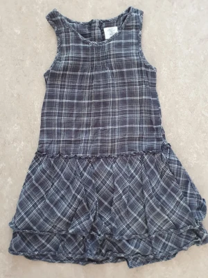 Klänning - Snygg grå  ärmlös klänning från H&M. i rutigt mönster. Klänningen har en avslappnad passform med volang i nederdelen och är tillverkad i mjuk bomull.