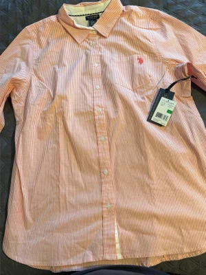 Randig skjorta från U.S. Polo Assn. - Säljer en snygg skjorta från U.S. Polo Assn. i vitt och rosa med tunna ränder. Skjortan har klassisk krage, knappstängning framtill och en liten broderad logga på bröstet. Perfekt för dig som gillar stilrena detaljer och bekvämt material.