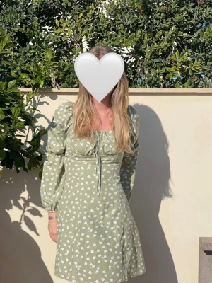 Grön blommig kortklänning  - Supersöt ljusgrön kortklänning från Shein med vitt blommönster. Klänningen har långa puffärmar, snörning framtill och en lätt v-ringad urringning. Perfekt för sommarens alla tillfällen och ger en romantisk vibe. I storlek S, bra skick. Säljer då den tyvärr blivit för lite för mig💞