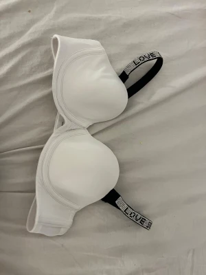 Vit  bh med strassband - Snygg vit bh med vadderade kupor och axelband dekorerade med strass och texten 'LOVE'. Perfekt för dig som vill ha något extra. Axelbanden är svarta undertill och prydda med glittrande detaljer. Materialet känns mjukt och bekvämt.