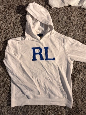 Vit hoodie från Polo Ralph Lauren🙌🤩 - Säljer en vit hoodie från Polo Ralph Lauren med blå RL-tryck på bröstet. Hoodien har en stor huva och en klassisk känguruficka framtill. Materialet är mjukt och bekvämt, perfekt för chill dagar. Stilen är enkel och sportig med ribbade muddar.🙌🤩