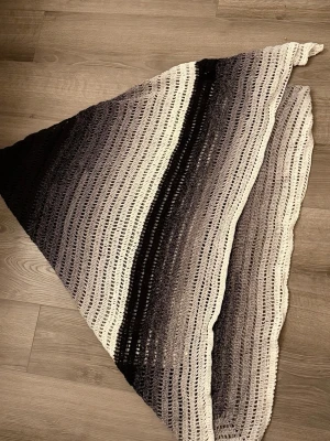 Handvirkad stor sjal  - En stor handvirkad sjal i triangelform med breda ränder i svart, grått och vitt. Sjalen har ett luftigt, hålmönstrat stickat material. Pris är för arbetstid + material