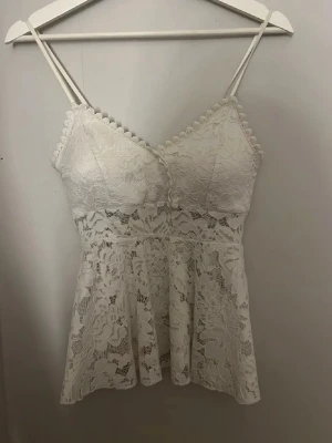 Vit spetslinnetopp - Säljer en superfin vit linnetopp med spetsdetaljer och smala axelband. Toppen har v-ringad hals och dekorativa kanter upptill. Perfekt för sommaren och ger en romantisk vibe till din outfit.