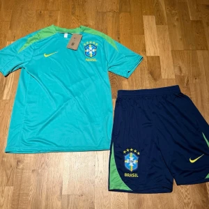 Brazil summer set turkosgrön - Säljer ett Brasilien träningsset från Nike med en turkosgrön t-shirt och mörkblå shorts. T-shirten har limegröna detaljer och Brasilien-emblem på bröstet, medan shortsen har samma emblem och Nike-logga. Perfekt för fotbollsträning eller sport.