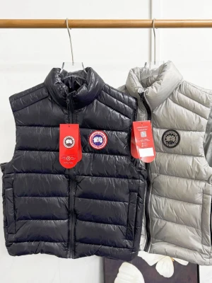 Canada Goose dunvästar svart & grå - Två snygga dunvästar från Canada Goose, en i svart och en i ljusgrå. Båda har hög krage, dragkedja framtill och klassiska logopatchar på bröstet. Västarna är quiltade och fyllda med dun för extra värme. Perfekt för lager-på-lager-stil.