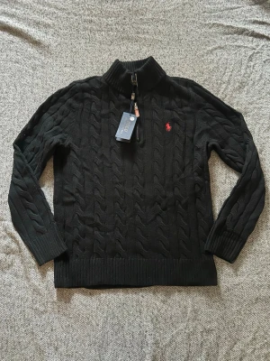 Kabelstickad Ralph Lauren tröja - Kabelstickad svart tröja från Polo Ralph Lauren med halv dragkedja och hög krage. Storlek M. Tveka inte på att höra av dig om du har frågor eller prisförslag! Fraktar samma dag✅