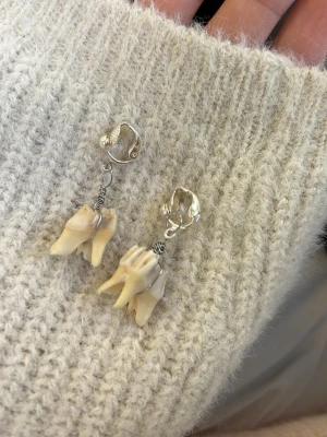 Unika örhängen med tänder och silver - Säljer ett par riktigt unika örhängen med clip-on fäste i silverfärgad metall och hängande detaljer av riktiga tänder. Örhängena har en edgy och alternativ stil som verkligen sticker ut. Perfekt för dig som gillar statement-smycken och vill ha något ingen annan har.