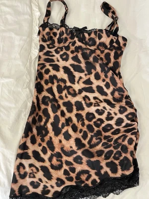 Leopardmönstrat nattlinne med spets - Snyggt nattlinne med leopardmönster i beige och svart. Justerbara axelband, liten rosett framtill och spetsdetaljer vid urringning och nederkant. Materialet känns mjukt och följsamt, perfekt för en chill kväll hemma.