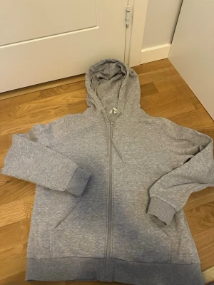 Grå hoodie med huva, storlek M - Säljer en enkel och stilren grå hoodie i storlek M. Hoodien har en klassisk huva med dragsko och ribbade muddar vid ärmslut och nederkant. Perfekt för en avslappnad och bekväm look. Materialet känns mjukt och skönt mot huden.