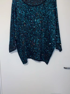 Svart paljettstickad tröja Phase Eight - Säljer en svart stickad tröja från Phase Eight täckt med glittriga paljetter i blått, grönt och lila. Tröjan har rund halsringning och trekvartsärmar, perfekt för dig som vill sticka ut lite extra.