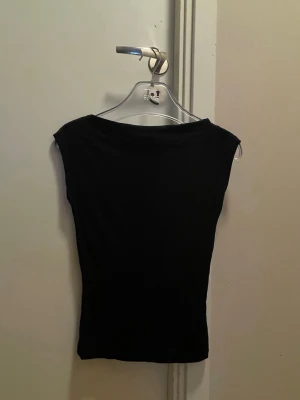 Svart ärmlös topp från Nelly - Snygg svart topp från Nelly i ärmlös modell. Toppen har en enkel och stilren design med rund halsringning och tight passform. Perfekt att matcha med jeans eller kjol för en clean look.