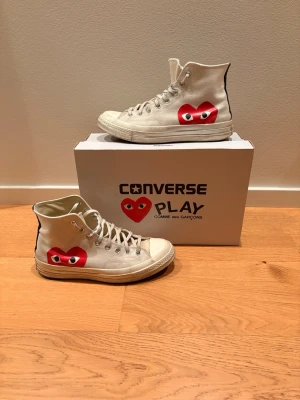 Converse x CDG Play vita high tops - Säljer ett par vita Converse x Comme des Garçons Play high top sneakers med det ikoniska röda hjärtat på sidan. Klassisk canvas, vita snören och gummisula. Perfekt för dig som vill ha en unik twist på klassiska Converse. De har tecken på användning som syns på bilderna. Hör av er vid minsta fundering! Nypris: 1295kr