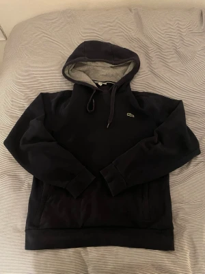 Lacoste hoodie - Säljer en tvärfet marinblå Lacoste hoodie i storlek S, den är använd men i bra skick. Skriv för frågor!🚀