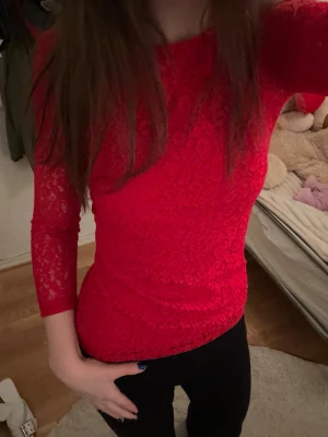Röd spetsblus med trekvartsärm - Snygg röd blus i spets med trekvartsärm och figurnära passform. Blusen har ett vackert blommigt spetsmönster och är perfekt för dig som vill sticka ut. Passar till både jeans och kjol för en trendig look.
