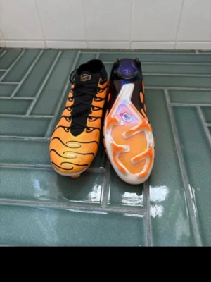 Orange och svart fotbollssko Nike - Säljer ett par snygga fotbollsskor från Nike i orange och svart med coola vågformade detaljer och svart snörning. Skorna har en modern design och slitstark sula med orange och vita inslag. Perfekta för dig som vill sticka ut på planen! Sparsamt använda några träningar , 8/10