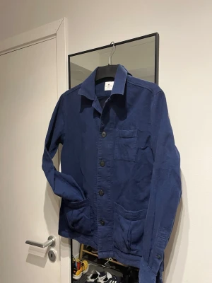 Marinblå overshirt från John Henric - Marinblå overshirt från John Henric med krage, tre framfickor och knäppning framtill. Tillverkad i ett mjukt bomullstyg som ger en avslappnad men snygg look. Passar perfekt för våren, samt sommaren.