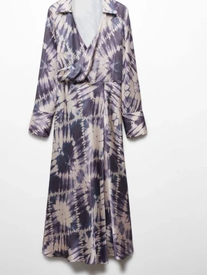 Långklänning med batikmönster Mango - Snygg långklänning med batikmönster i blått lilla grått och beige. Klänningen har omlottmodell, v-ringning och långa ärmar. Tillverkad i ett mjukt och följsamt material som ger en skön passform och ett coolt uttryck.