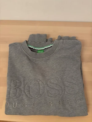 Grå sweatshirt från Hugo Boss - Snygg grå sweatshirt från Hugo Boss med broderad logga framtill. Tröjan har rund halsringning, ribbade muddar och är tillverkad i mjukt material. Perfekt för en avslappnad och stilren look.