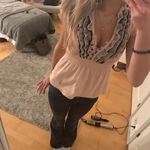 Rosa blus med volangdetaljer - Säljer en söt rosa blus med volangdetaljer och v-ringning. Blusen har en smockad midja som ger en fin passform och ärmlös design. Perfekt för en stilren look!