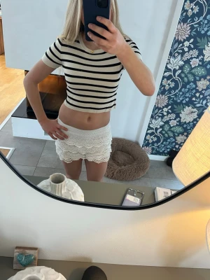 Randig croppad topp Gina Tricot - Säljer en croppad topp från Gina Tricot i svart och vitt med klassiskt randigt mönster. T-shirten har korta ärmar och rund halsringning. Perfekt till jeans eller kjol för en trendig look.