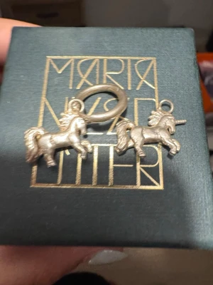 Unicorn örhängen från Maria Nilsdotter - Säljer ett par unika örhängen från Maria Nilsdotter i silverfärgad metall. Örhängena har detaljerade enhörningshängen som ger en lekfull och magisk vibe. Perfekta för dig som vill sticka ut med något annorlunda och kreativt. Tyvärr har en av ringarna tappats bort men de går lätt o köpa ny likadan 