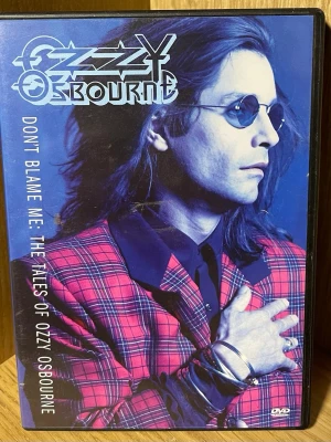 Ozzy Osbourne DVD Don't Blame Me - DVD med titeln 'Don't Blame Me: The Tales of Ozzy Osbourne'. Omslaget har en blå bakgrund med Ozzy i röd- och svartmönstrad kavaj. Innehåller dokumentär, musikvideor och intervjuer om Ozzy Osbournes liv och karriär. DVD-fodral i plast.
