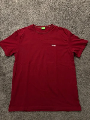 Röd t-shirt Hugo BOSS strl L - Snygg röd t-shirt från BOSS med diskret logga på bröstet. Klassisk rund halsringning och korta ärmar. Tillverkad i mjuk bomull som känns skön mot huden. Använd ytterst få gånger och har inga defekter. Skriv gärna vid frågor eller funderingar!😃✅