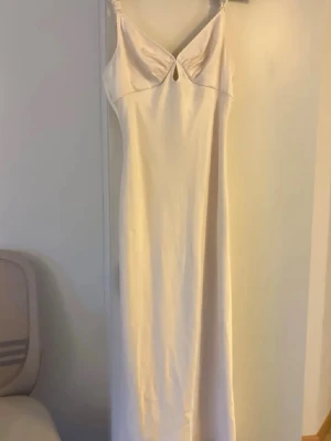 Adoore Ljus långklänning med smala axelband - Elegant långklänning i ljus beige med smala axelband och en liten nyckelhålsdetalj framtill. Klänningen har en figurnära passform och är tillverkad i ett mjukt, slätt material som ger ett stilrent intryck. Perfekt för sommarens alla tillfällen. Storlek 38