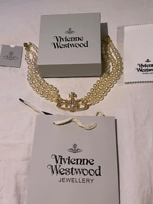 Vivienne Westwood pärlhalsband - Guld - Ikoniskt halsband från Vivienne Westwood med tre rader vita pärlor och ett stort guldfärgat Orb-hänge. Halsbandet har klassisk och lyxig känsla med detaljer i guld och pärlemor. Perfekt för dig som vill sticka ut med ett statement-smycke.