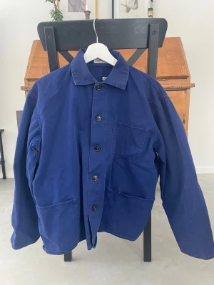 Blå vintage overshirt med stora fickor - Stilren blå overshirt i kraftig bomull med tre stora utanpåfickor och klassisk krage. Rak passform och knäppning med svarta knappar framtill. Perfekt för lager-på-lager och enkel att styla till olika outfits.