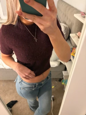 Vinröd stickad topp Gina Tricot - Mysig vinröd stickad topp från Gina Tricot i alpackablandning. Kortärmad modell med rund hals och mjuk, fluffig känsla. Perfekt att styla med jeans eller kjol för en trendig look. Lappen har blivit missfärgad av brun utan sol, annars nyskick