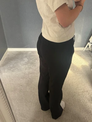 Svarta kostymbyxor - Säljer ett par svarta kostymbyxor med rak passform. Byxorna har låg midja och klassisk look, perfekta till en stilren outfit. Materialet är en mjuk och följsam textil som ger en snygg siluett.