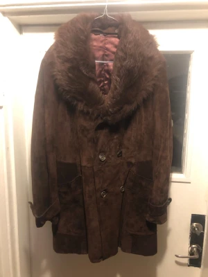 Dubbelknäppt kappa / rock Jofama vintage. Mocka.  - Säljer en brun vintage kappa i mocka med bred löstagbar krage i fuskpäls. Dubbelknäppt framtill med stora knappar och två rymliga fickor fram, 1 innerficka. Extremt bra skick utan fläckar eller synligt slitage.