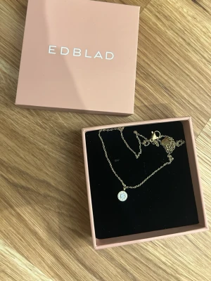 Guldhalsband med rund berlock från Edblad - Snyggt guldhalsband från Edblad med en rund berlock dekorerad med gnistrande stenar. Kedjan är tunn och elegant, perfekt för att lyfta vilken outfit som helst. Kommer i original ask.