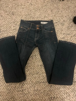Mörkblå bootcut jeans från Bershka - Snygga mörkblå bootcut jeans från Bershka med klassisk femficksdesign och kontrastsömmar. Jeansen har en hög midja och stängs med knapp och dragkedja. Perfekta för en trendig och avslappnad stil.