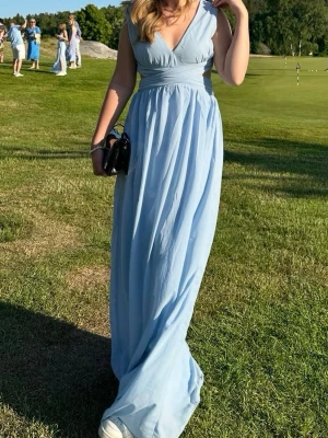 Ljusblå långklänning med öppen rygg - Snygg ljusblå långklänning med v-ringning och breda axelband. Från Nelly i storlek 36